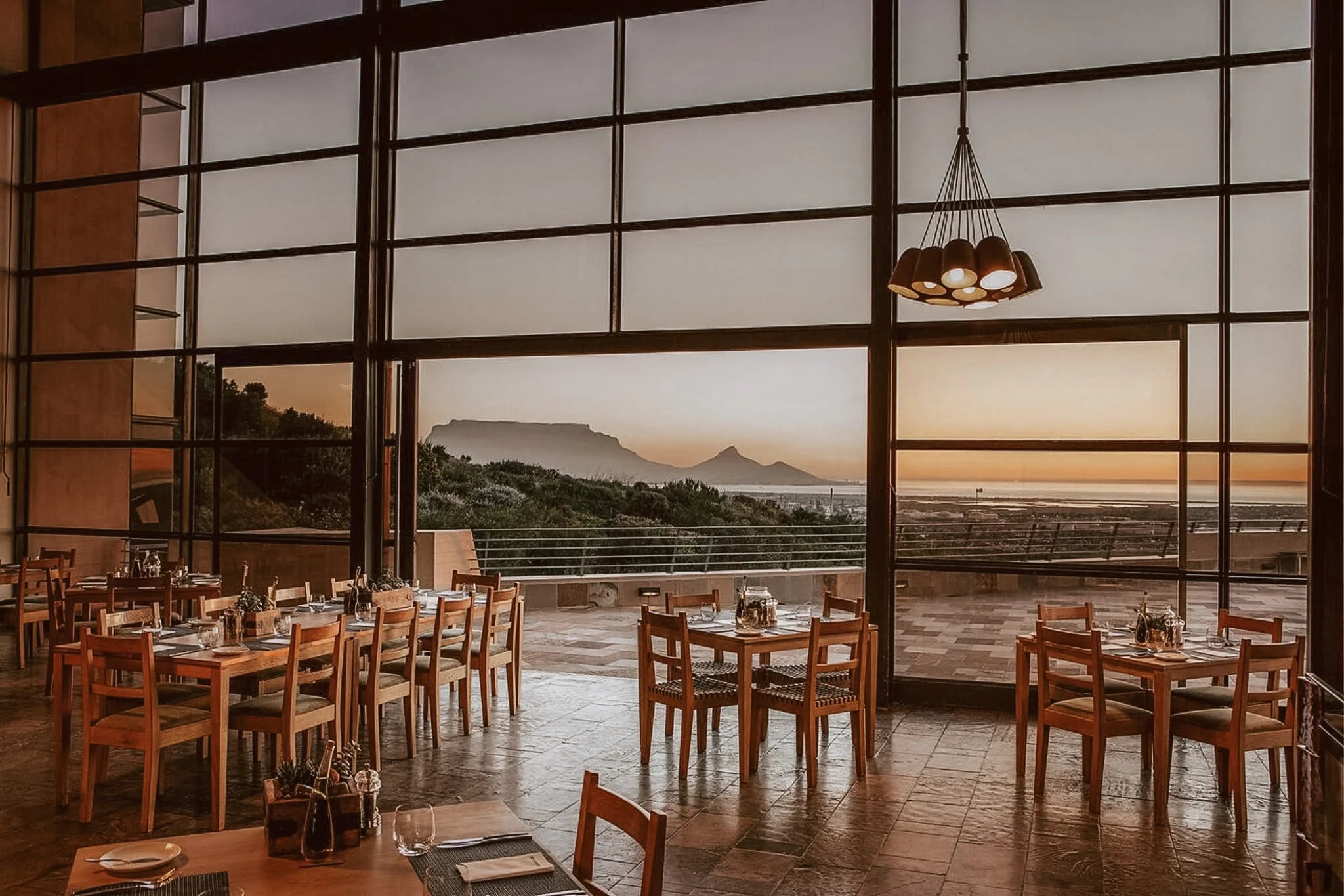 Blick aus dem erstklassigen Restaurant auf die Terasse bei Sonnenuntergang. Im Hintergrund erkennt man die Silhouette des Tafelbergs