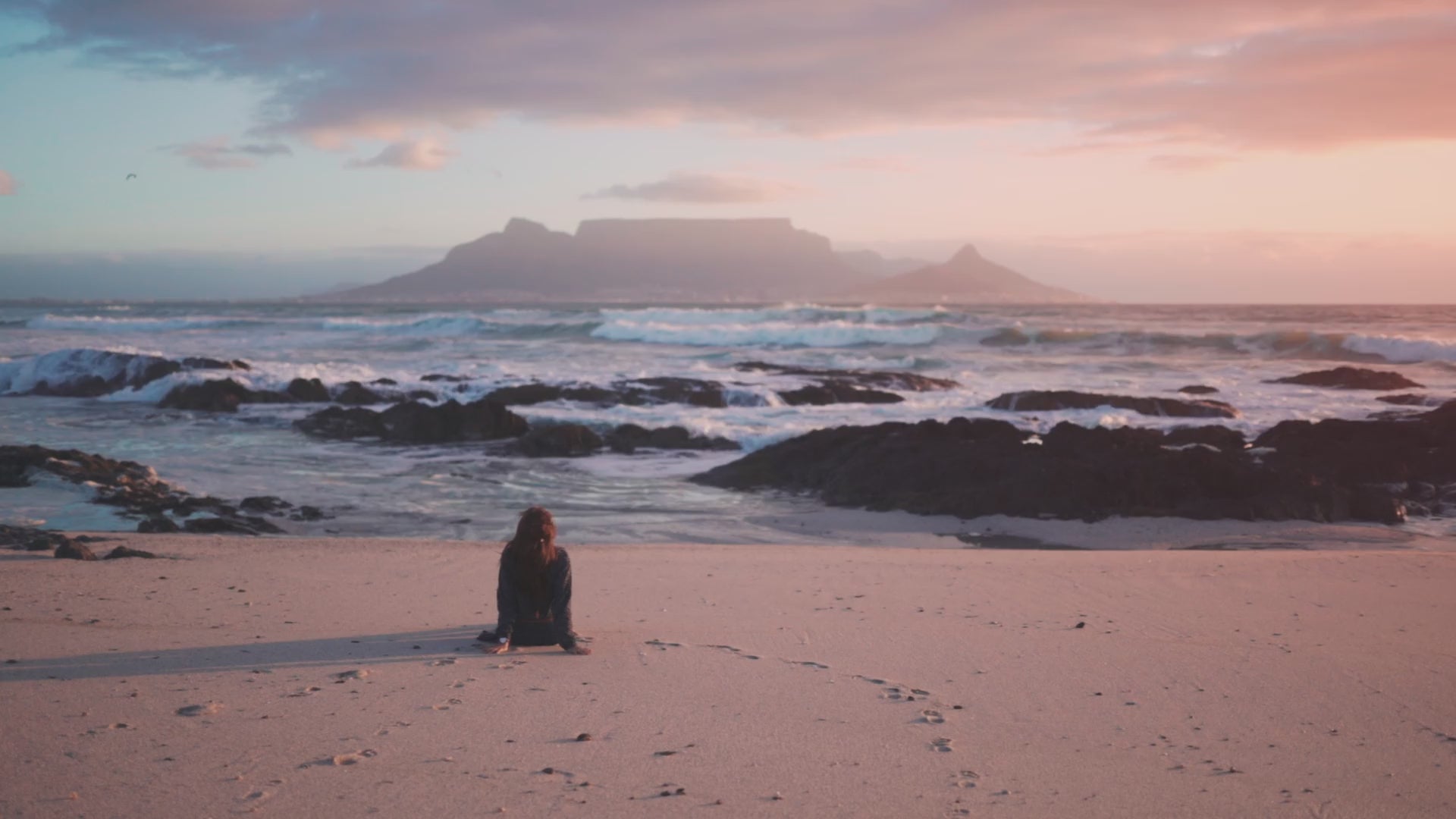 Load video: Woman sitting by the sea looking at Table Mountain